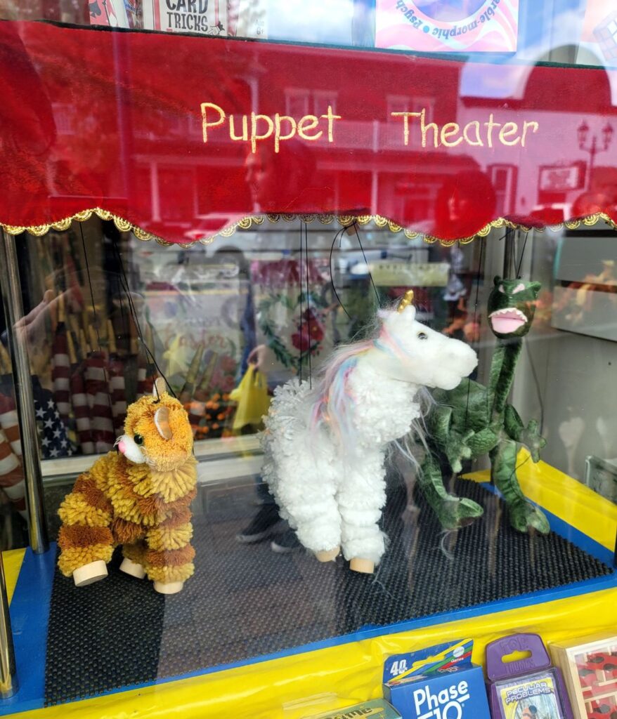 Yarn marionette puppets — orange cat, white unicorn, and green dragon — in a Main Street toy store puppet theater display in Frankenmuth, Michigan.