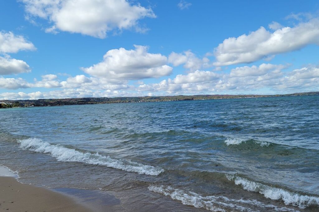 The sandy swimming area at Suttons Bay Municipal Beach on Grand Traverse Bay, showing the calm water and nearby park amenities.