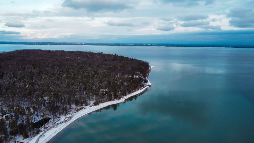 Aerial view of Grand Traverse Bay shoreline with snow-covered forests in winter near Traverse City Michigan.
