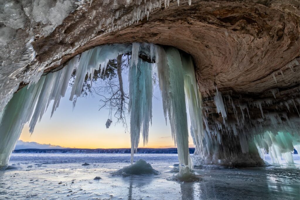 Frozen ice caves at sunset along Lake Superior in Michigan's Upper Peninsula, with massive icicles hanging from sandstone overhangs in winter
